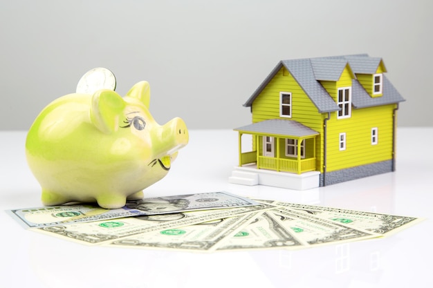 Piggy bank for money and a house model with dollars on a white background buying a property the concept of buying and selling houses and apartments