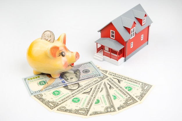 Piggy bank for money and a house model with dollars on a white background buying a property the concept of buying and selling houses and apartments