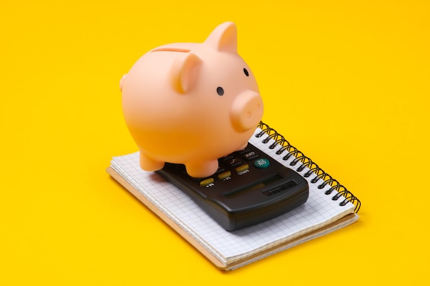 Piggy bank, notebook and calculator on yellow