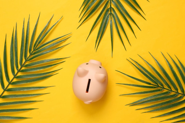 Piggy bank and palm leaves on yellow background Tropical composition Top view Flat lay