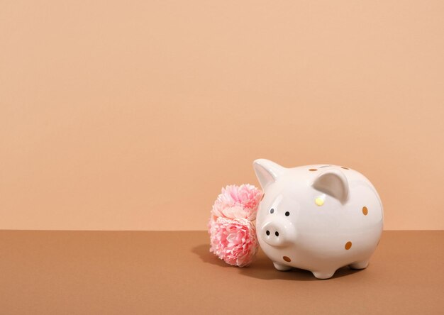 Photo piggy bank and pink flowers on a beige background copy space for text piggy bank savings concept