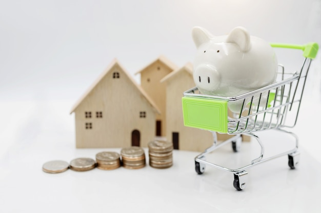 Piggy bank on shopping cart with coins stack and house.  Concept of investment in housing.