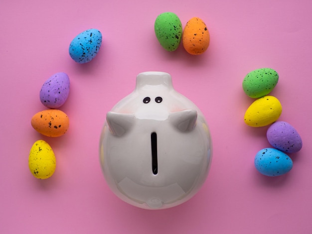 Piggy bank surrounded by colorful Easter eggs on pink background