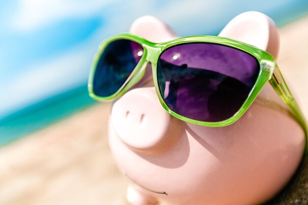 Photo piggy bank wearing sunglasses relaxing at the beach