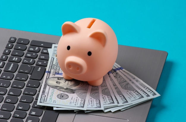 Piggy bank with 100 dollar bills on laptop keyboard closeup