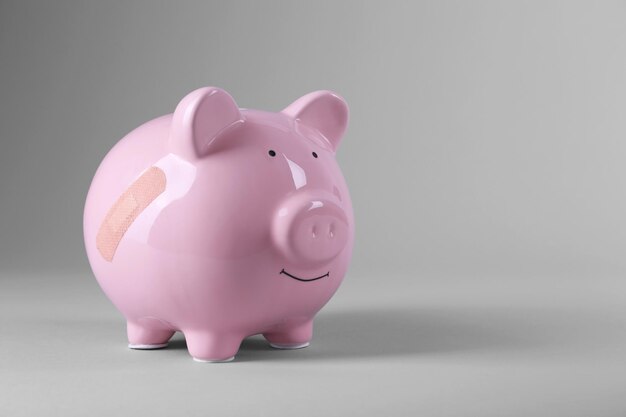 Piggy bank with adhesive bandage on grey background