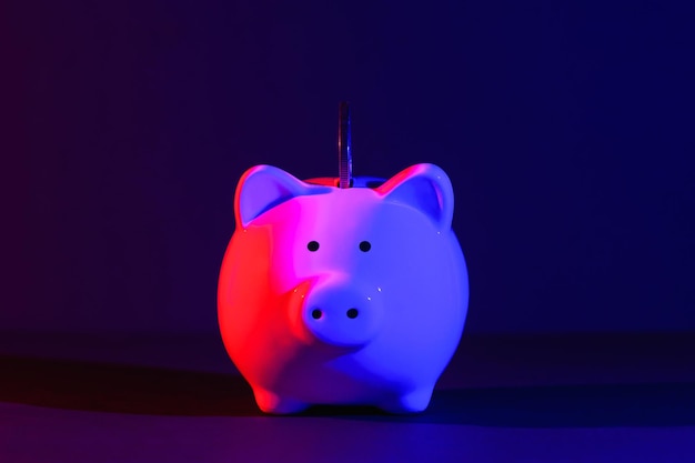 Piggy bank with coin on a dark background redblue backlight Banking concept Bright neon lights