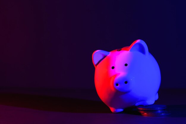사진 빨간색 파란색 백라이트 뱅킹 개념 밝은 네온 불빛으로 어두운 배경에 동전이 있는 돼지 저금통