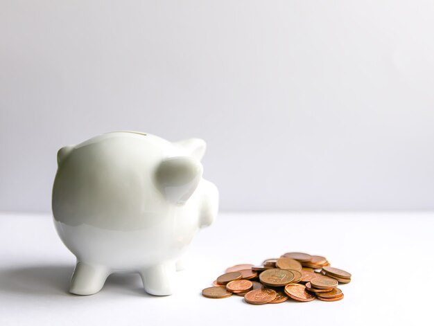 Piggy bank with coins. White ceramic moneybox.