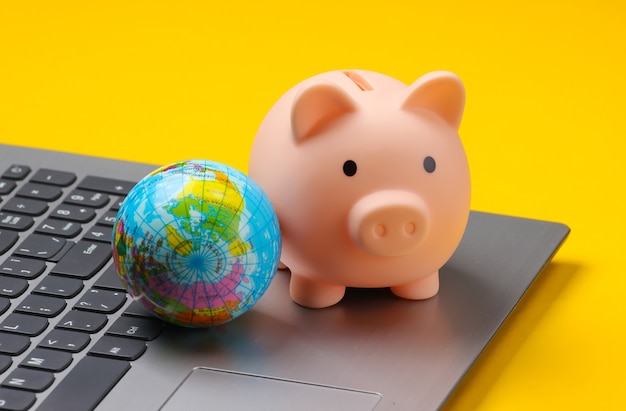 Photo piggy bank with globe on laptop keyboard,  yellow.