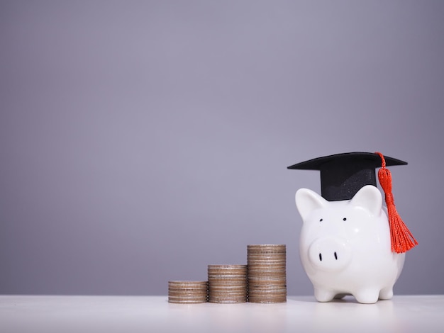 Фото Копилка с выпускной шляпой и стопкой монет концепция экономии денег на образование, студенческий кредит, стипендия, плата за обучение в будущем