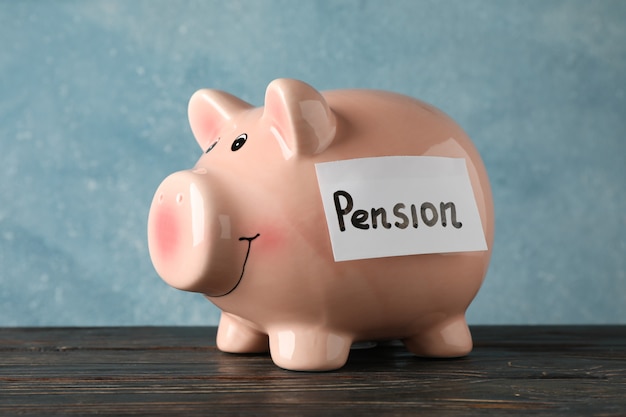 Piggy bank with inscription Pension against blue surface