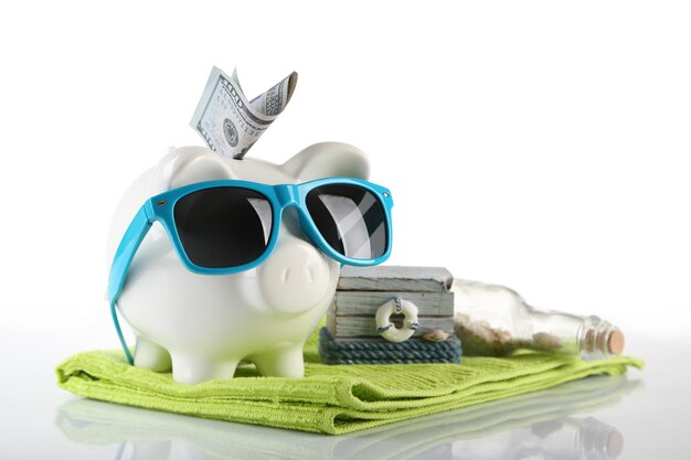 Piggy bank with inserted dollar banknote towel and sunglasses isolated on white Holiday money concept