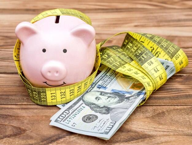 Piggy bank with measuring tape and money on wooden background