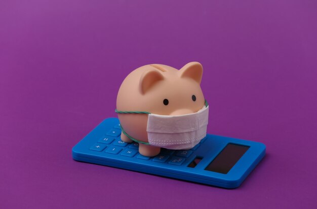 Piggy bank with medical mask and calculator on purple background. Economic disease. Financial crisis. Covid-19 pandemic