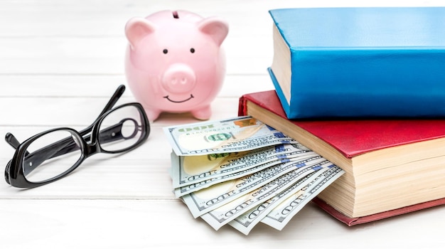 Piggy bank with money glasses and stack of books on the table