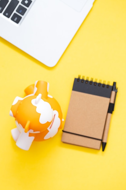 Piggy bank with notepad and computer on yellow background