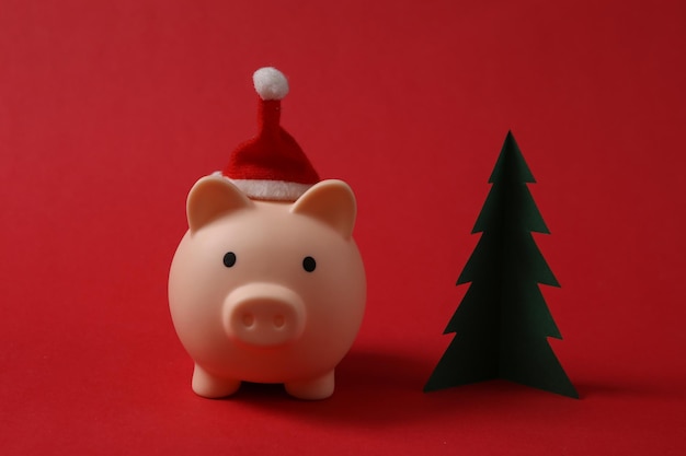 Piggy bank with santa hat and Christmas tree on red background Christmas concept