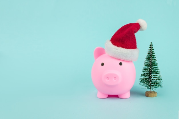 Photo piggy bank with santa hat with christmass tree on blue background. symbol of new year.