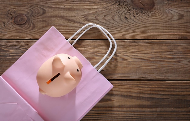 Piggy bank with shopping bag on wooden background Top view