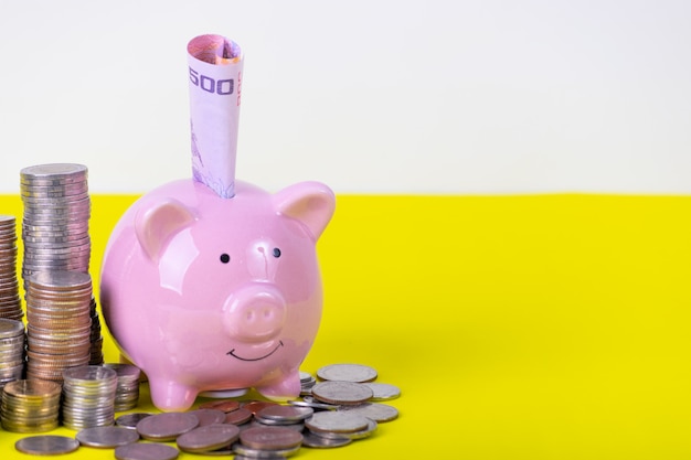 Piggy bank with stack of coin on yellow table. Financial or Saving money concept.