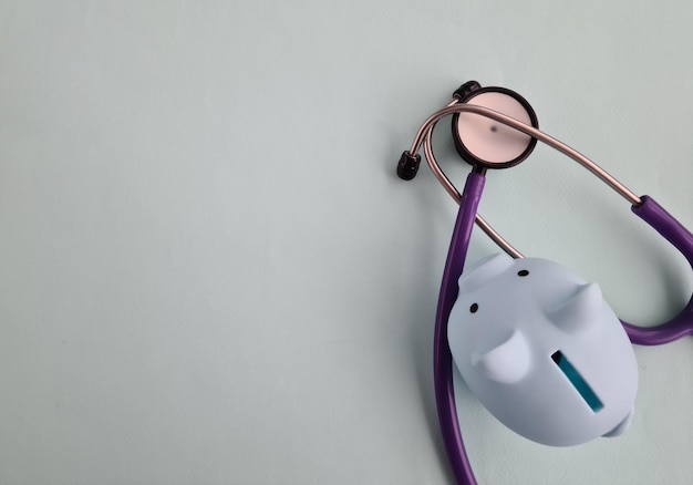 Piggy bank with stethoscope on blue background with copy space