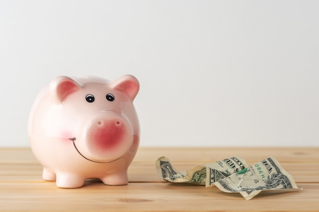 Piggy bank on a wooden table with crumpled dollar banknote