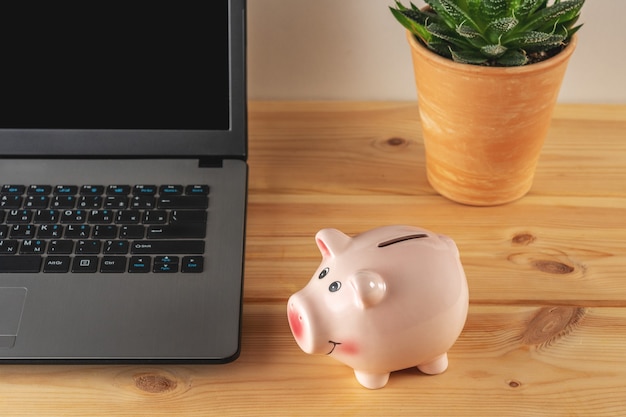Piggy bank on a wooden table with a laptop