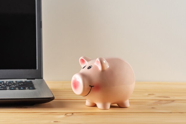 Piggy bank on a wooden table with a laptop.