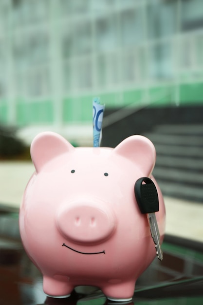 Piggy money box with cash and key on car bonnet at the street