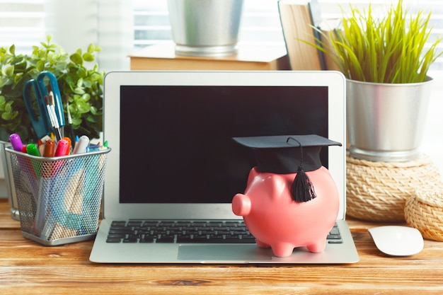 Piggy money box with laptop on wooden table