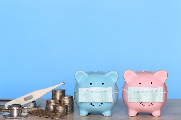 Piggy with wearing protective medical mask and thermometer with stack of coins money on wooden background, Save money for Medical insurance and Health care concept