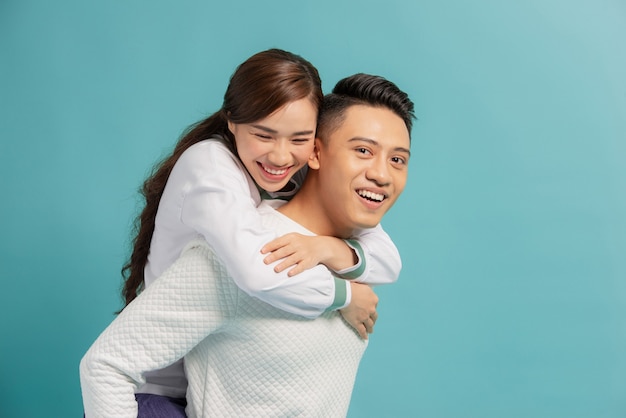 Piggyback ride. Young man carrying girlfriend on his back, blue with copy space.