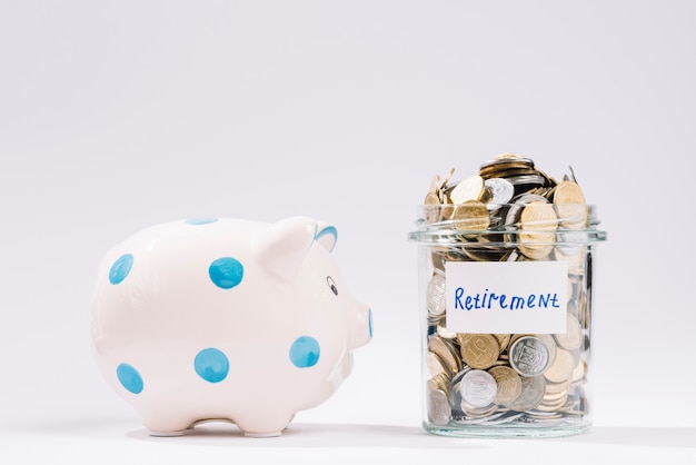 Piggybank near retirement container full of coins on white backdrop