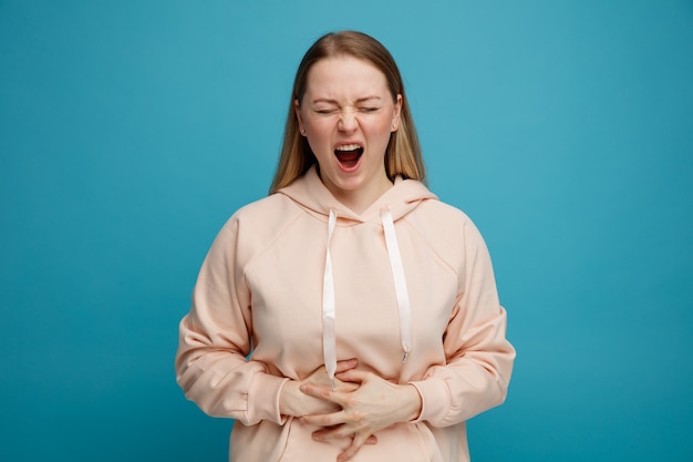 Pijnlijke jonge blonde vrouw die handen op buik houdt die met gesloten ogen schreeuwen