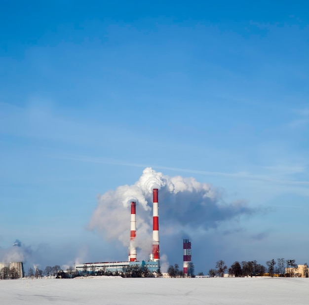 Pijpen van een thermische elektriciteitscentrale van een onderneming die brandstof verbrandt en een grote hoeveelheid rook en emissies in de atmosfeer uitstoten, industriële pijpen met witte rook in de winter