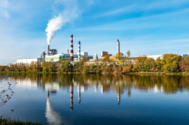 Pijpen van houtbewerking onderneming fabriek zagerij in de buurt van rivier Luchtvervuiling concept Industrieel landschap milieuvervuiling afval van thermische elektriciteitscentrale