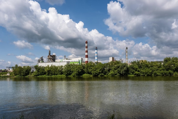 Pijpen van houtbewerkingsbedrijfsfabriek zagerij in de buurt van rivier en jongen op kajak Luchtvervuilingsconcept Industrieel landschap milieuvervuiling afval van thermische elektriciteitscentrale