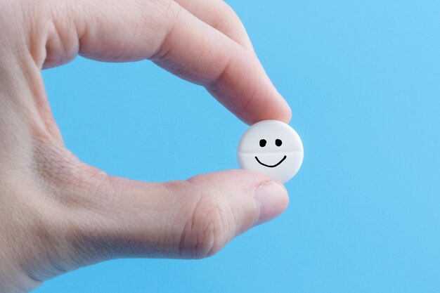 Pil met een emoticon in de hand op een blauwe achtergrond Gezondheidsbehandeling en preventie