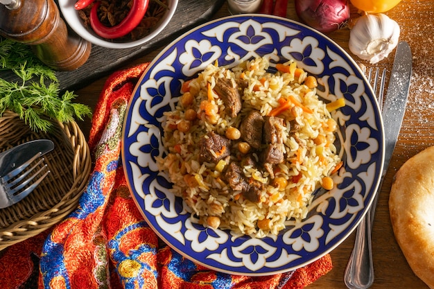 Pilaf met lamsvlees. Traditionele oosterse warme schotel van rijst, lamsvlees en gele wortelen met knoflook, rozijnen, kikkererwten en kurkuma in een bord met een nationaal Oezbeeks ornament.