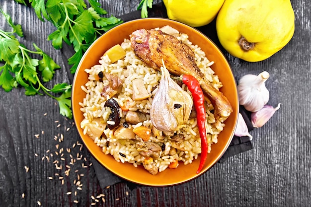 Pilaf of rice, duck, quince, carrots with garlic, onion, prunes and spices in a plate on a towel on wooden board background from above