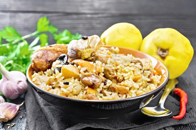 Pilaf van rijst, eend, kweepeer, wortelen met knoflook, ui, pruimen en kruiden in een bord op een theedoek op houten plank achtergrond