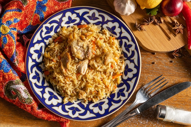 Photo pilaf with chicken. traditional oriental hot dish of boiled rice, chicken meat, vegetables and spices in a plate with a national uzbek ornament.