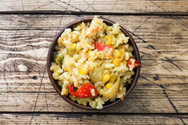 Pilaf with vegetables and chicken in wooden bowl