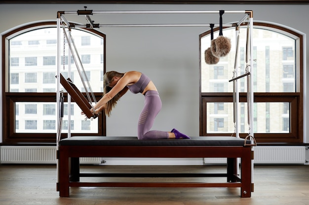 Pilates aerobics instructor woman in fitness exercise on cadillac reformer, musculoskeletal system training on modern reformer simulator.