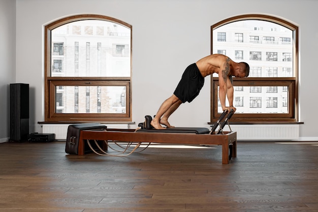 Photo pilates reformer workout exercises man at gym indoor.
