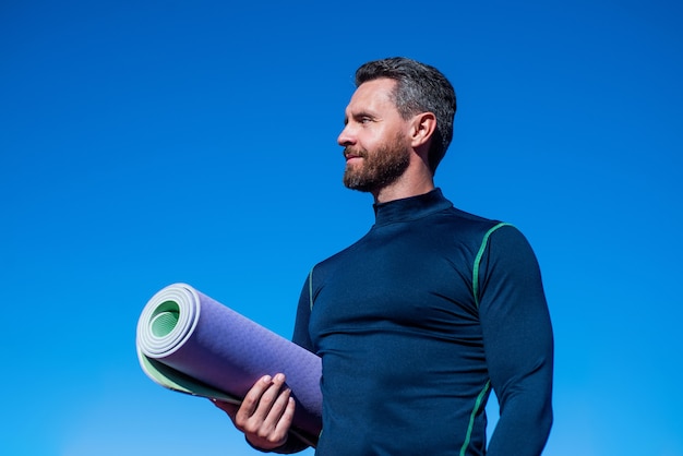 Pilates trainer with yoga mat on sky background, workout.