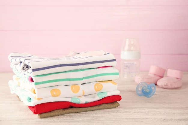 Pile of baby clothes on pink wooden background