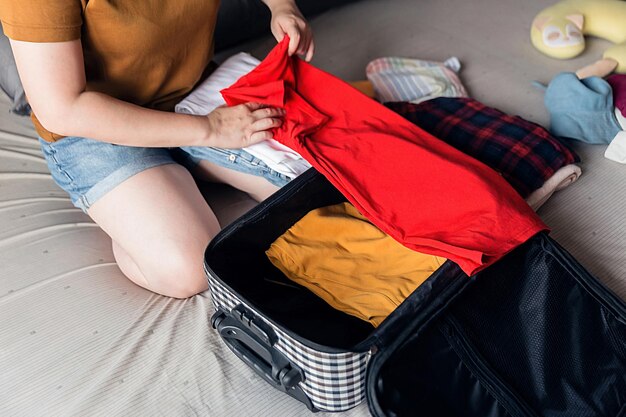 휴가 여행을 위해 포장할 준비가 된 침대 위의 다채로운 옷과 수하물 더미