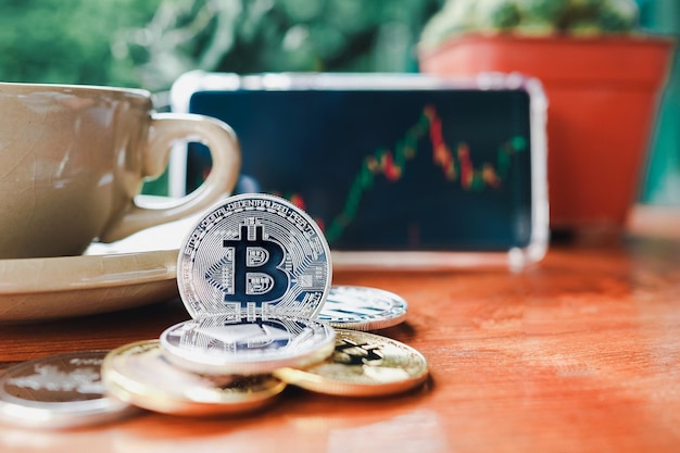 Photo pile of bitcoin or coins of cryptocurrency symbol and smartphone showing stock chart in cafe